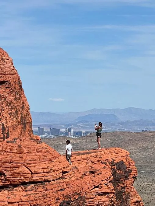 Guests taking photos on a red rock outcrop with the Las Vegas Strip far below