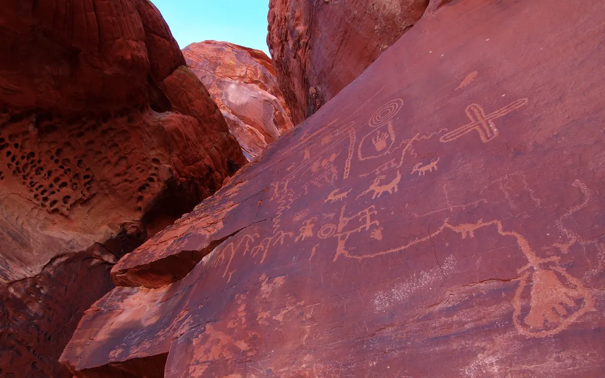 Ancient petroglyphs of bighorn sheep and human figures carved into dark red sandstone at Atlatl Rock